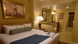 A hotel room with a large bed, a bedside table with a lamp, a mirror, and a bathroom visible in the background. - Great Value (Lake Buena Vista)