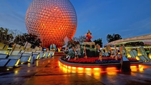A large spherical building with a textured surface, surrounded by a landscaped area with a central statue and seating arrangements. - Great Value (Lake Buena Vista)