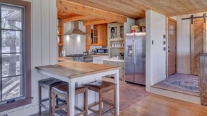 Een moderne keuken met houten balken, een centraal eiland met krukken, een roestvrijstalen koelkast en een magnetron.