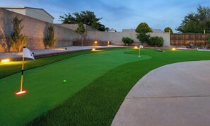 Un jardin bien entretenu, doté d’une pelouse artificielle, d’un green d’entraînement et d’une terrasse en béton.