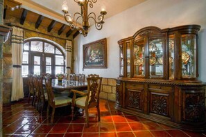 A dining area with a wooden table, chairs, a chandelier, a cabinet with glass doors, and a painting on the wall.