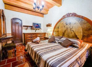 Ein Hotelzimmer mit einem großen Bett, einem Holz-Kopfteil, einem Fernseher, einem Holzschrank und einem kleinen Tisch mit einer Lampe.