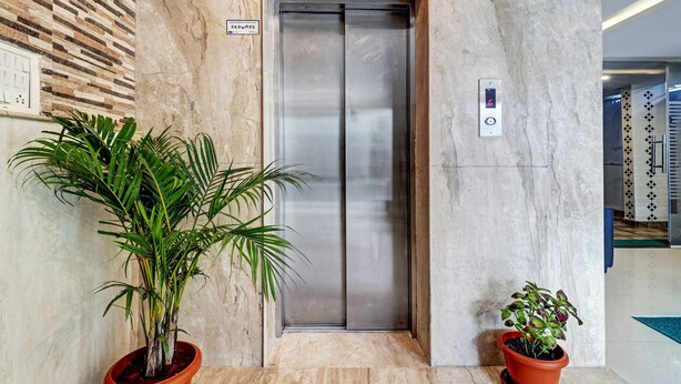 An elevator with a digital display, a marble wall, and two potted plants. - Treebo Elite Premium Homes (Bengaluru)