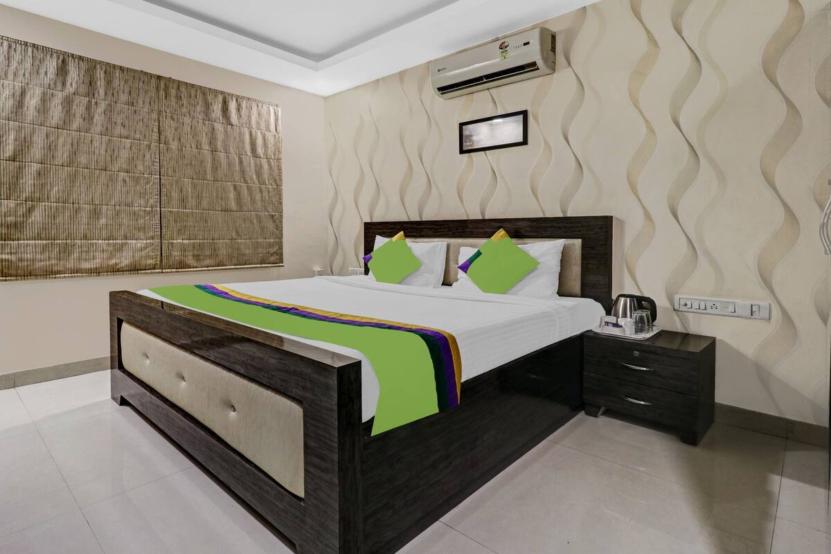 A bedroom with a bed, bedside tables, an air conditioning unit, and a window with blinds.