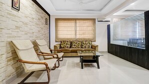 A living room with a sofa, two armchairs, a coffee table, and a large window with blinds. - Treebo Elite Premium Homes (Bengaluru)