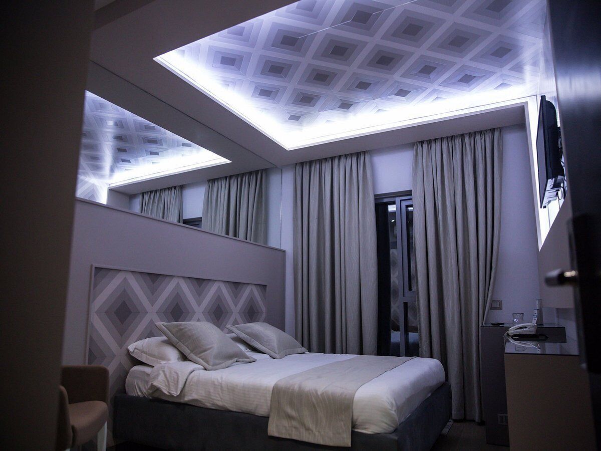 Ein modernes Hotelzimmer mit einem großen Bett, einem Kopfteil mit geometrischem Muster, einer Dachfensterdecke und einem Spiegel an der Wand.