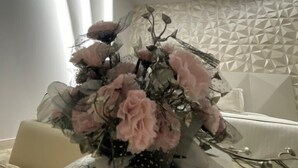 Une pièce dont un mur est orné d’un motif géométrique, un vase contenant des fleurs roses et un objet sphérique texturé posé sur une table.