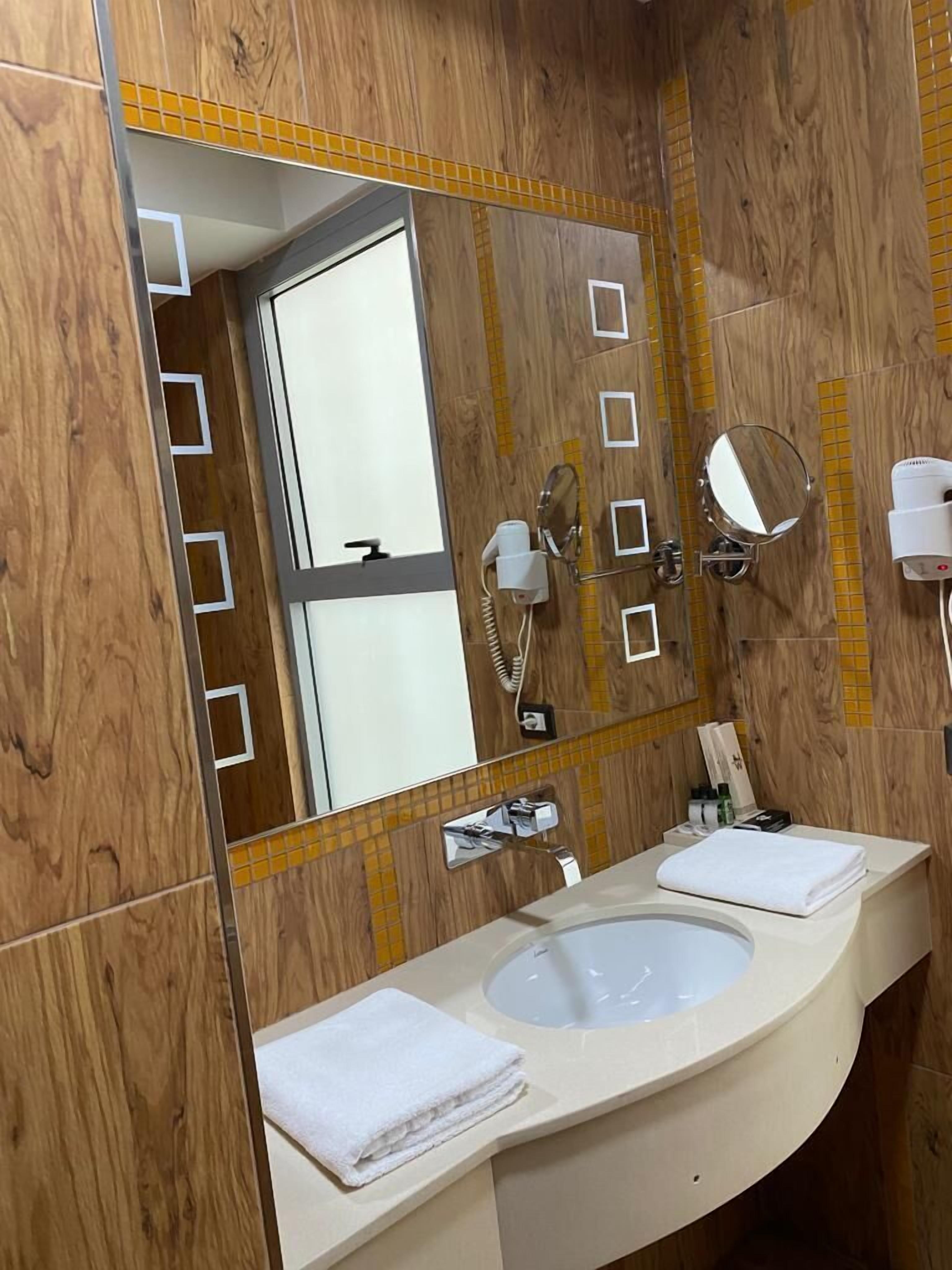 A bathroom with wooden paneling, a large mirror, a sink, and a towel.