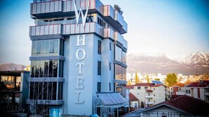 Un hôtel moderne, facilement reconnaissable grâce à son grand panneau lumineux indiquant « HÔTEL », avec une architecture à plusieurs étages, de grandes fenêtres et un toit plat.