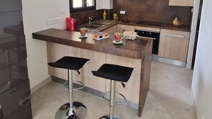 A modern kitchen with a central island, two bar stools, a built-in oven, and a window above the sink.