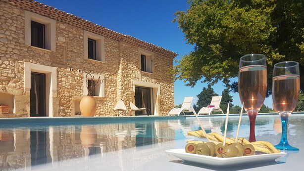 A stone building with a pool, lounge chairs, and a plate of olives and breadsticks.