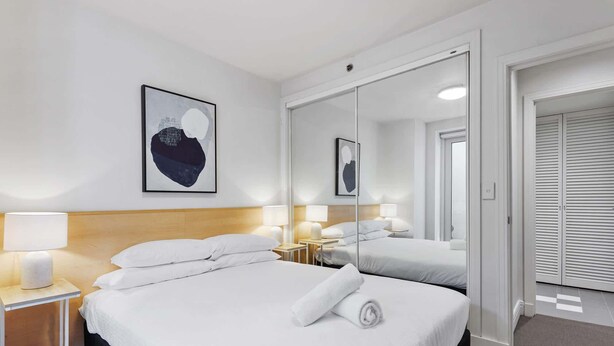 Ein Hotelzimmer mit Bett, Nachttischen, Lampen, einem Spiegel und einer Tür.