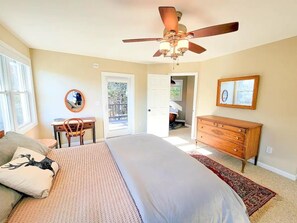 A bedroom with a large bed, a ceiling fan, a dresser, a desk, and a chair.