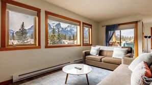 A living room with a sofa, a coffee table, and large windows with a mountain view. - Bluebird - Spacious Luxury, Shared Rooftop Hot Tub (Canmore)