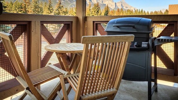 A balcony with a view of mountains, a grill, and two wooden chairs. - Bluebird - Spacious Luxury, Shared Rooftop Hot Tub (Canmore)