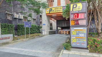 A parking entrance with a digital parking meter, a sign indicating parking rates, and a gated entrance to a building.