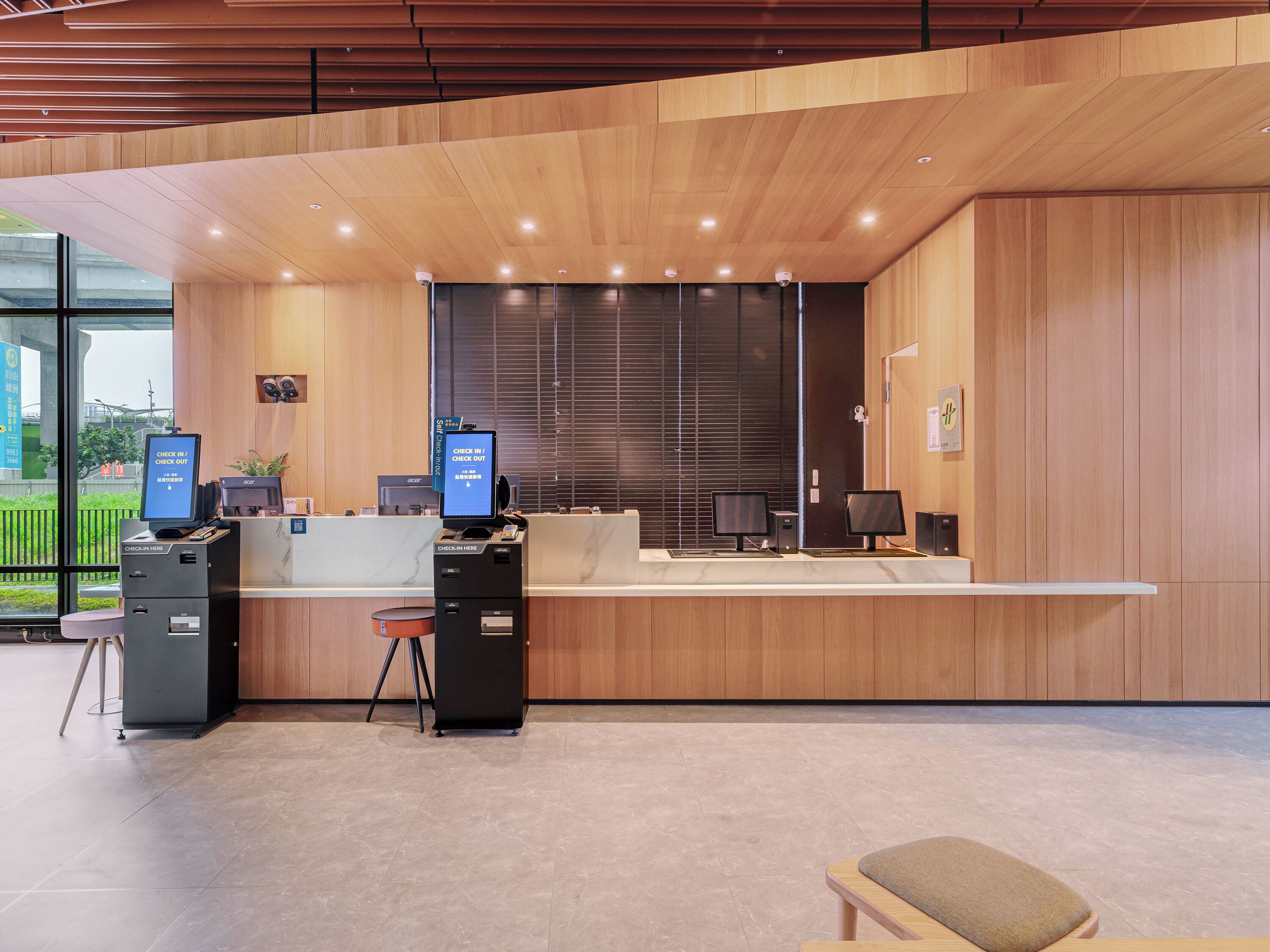 Een modern receptiebalie met een in-/uitcheckkiosk, een computerscherm en een zithoek met een comfortabele bank.