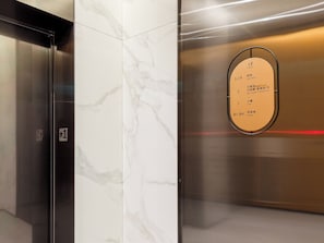 Interior de elevador com parede de mármore e sinalização com números e nomes de quartos.