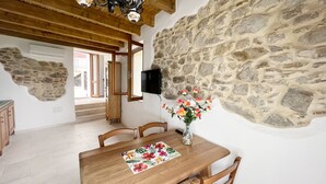 A dining area with a wooden table, chairs, and a vase of flowers. A stone wall and a television are also visible. - Premium Townhouse: Panoramic Rooftop Terrace with Nature and Ocean Views (Posada)