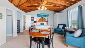 Une chambre avec un plafond en bois, un lit avec une tête de lit, un canapé bleu, une table à manger avec des chaises et un ventilateur de plafond.