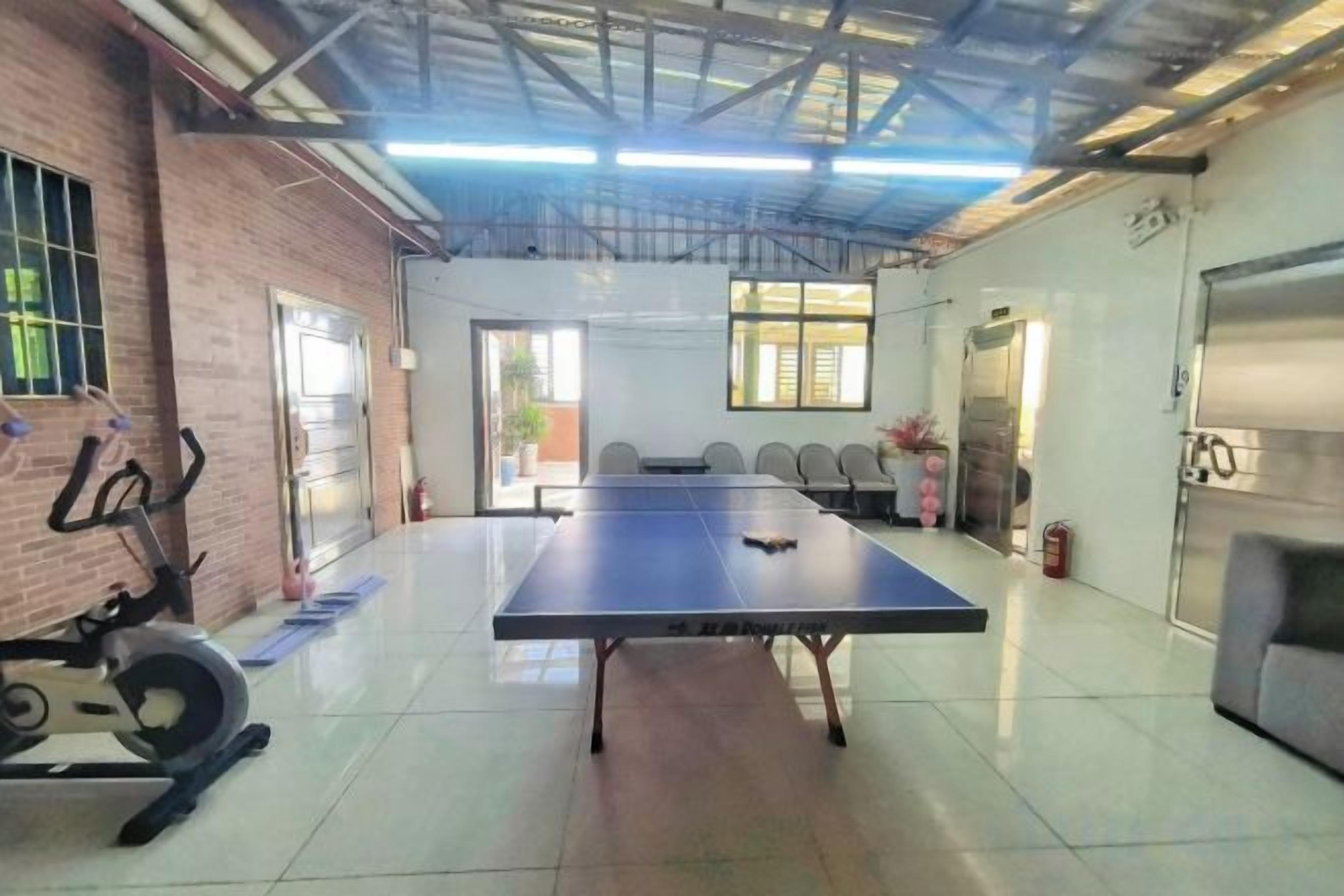 A spacious room with a ping pong table, exercise equipment, and a large window providing natural light.