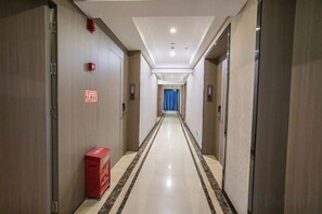A hotel corridor with doors on both sides, a red trash bin, and a blue curtain at the end. - Di Hao Hotel (Wuchuan)