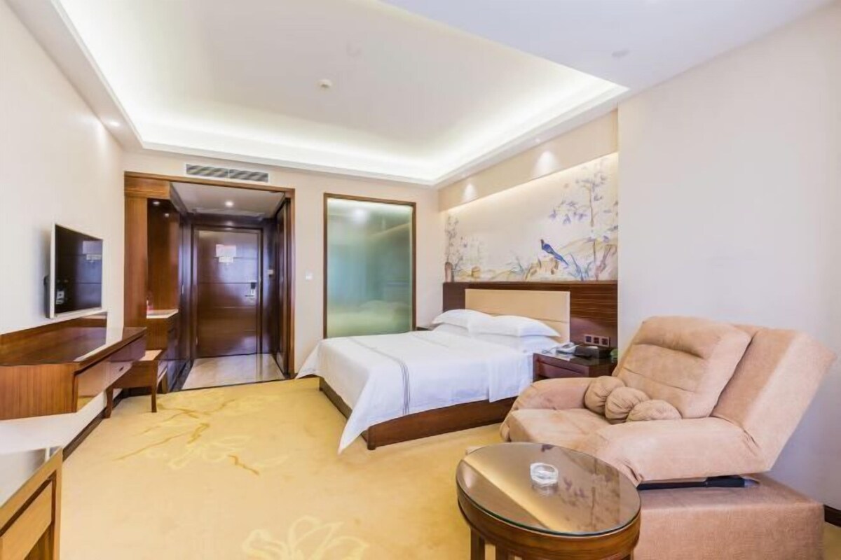 A hotel room with a bed, a sofa, a small table, and a TV.