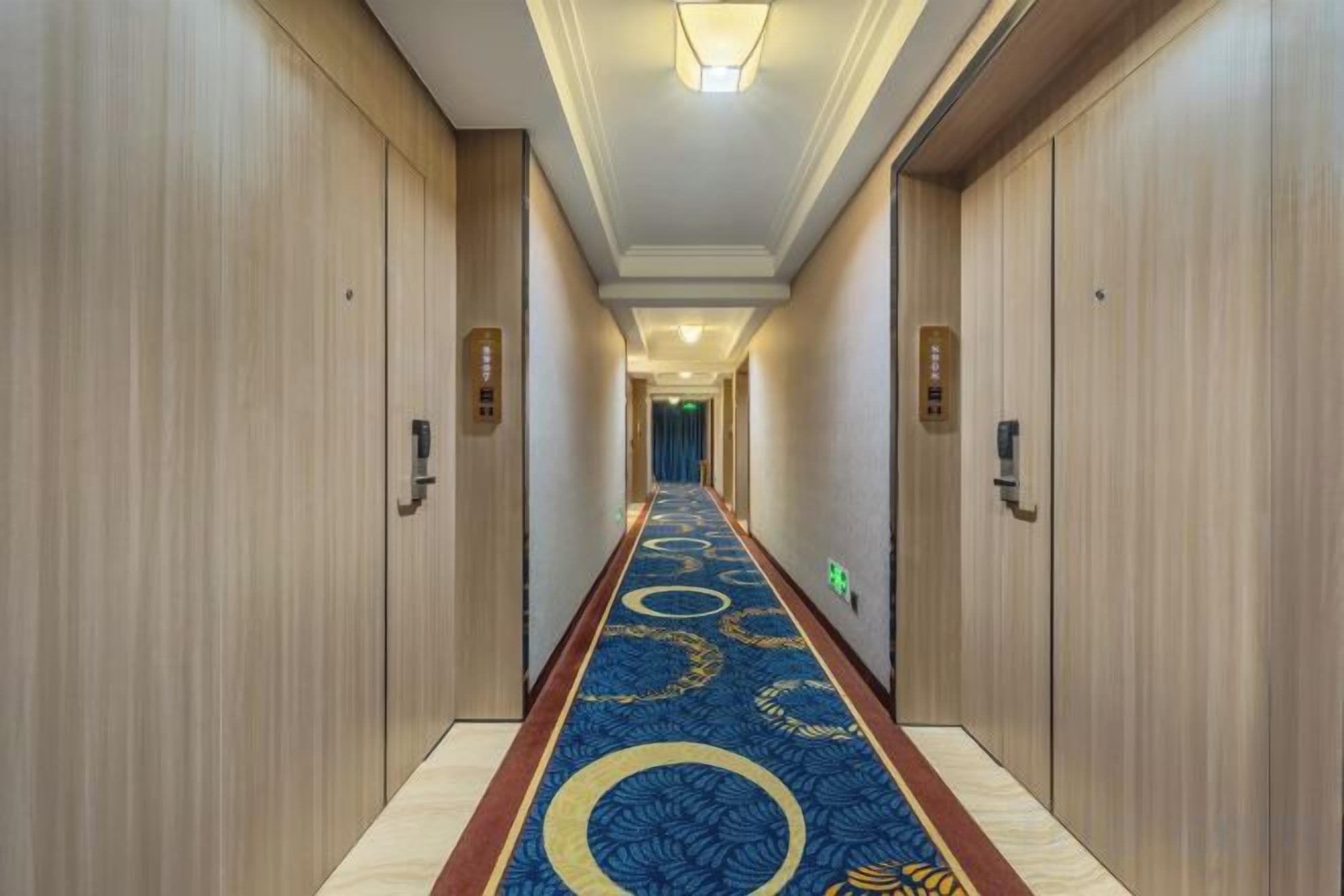 A hotel hallway with wooden doors, a blue carpet with circular patterns, and a light fixture on the ceiling.