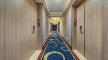 A hotel hallway with wooden doors, a blue carpet with circular patterns, and a light fixture on the ceiling.