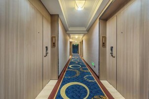 Un pasillo de hotel con puertas de madera, alfombra azul con diseños circulares e iluminación en el techo.