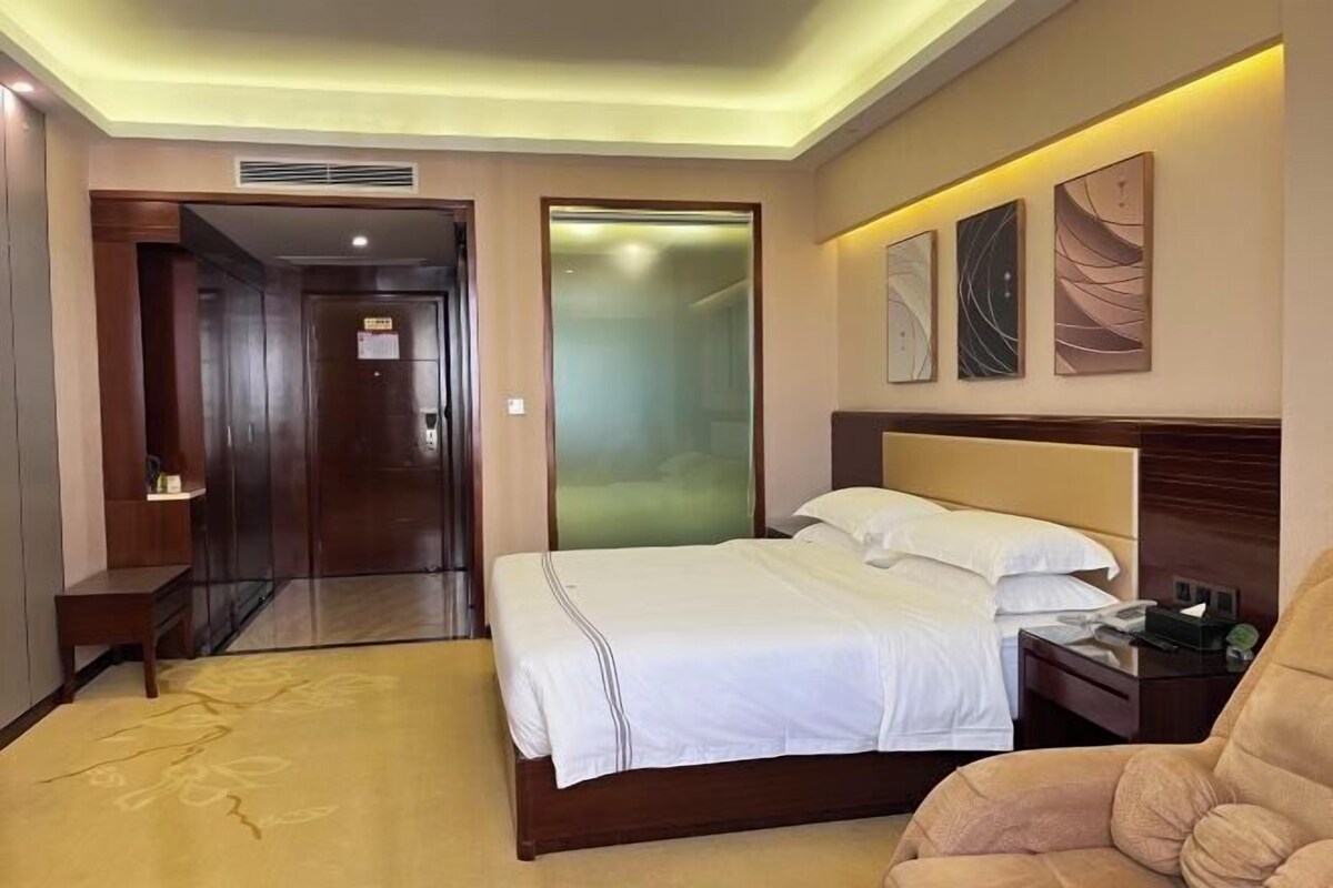 A hotel room with a bed, a chair, a nightstand, and a wall with artwork.
