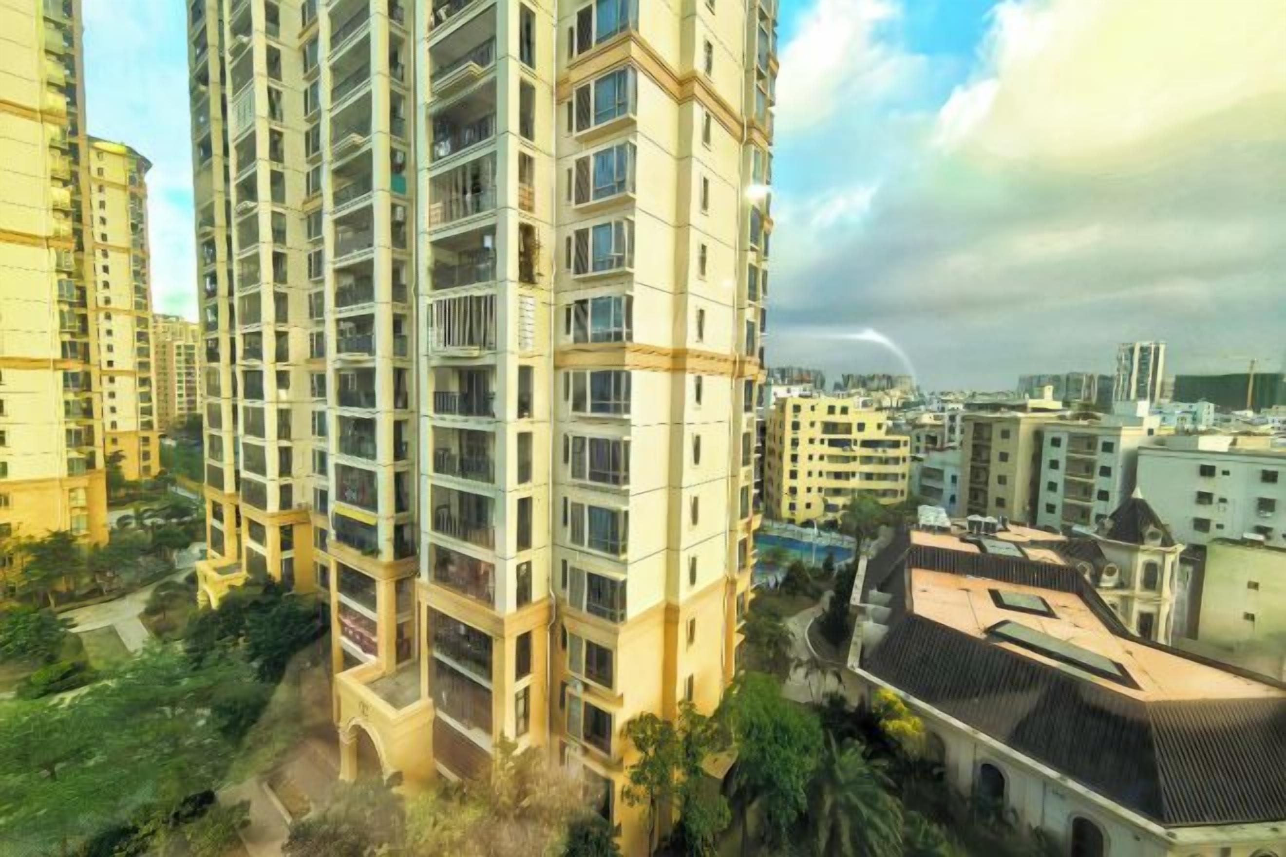 A high-rise residential building with multiple balconies, surrounded by other buildings and greenery.