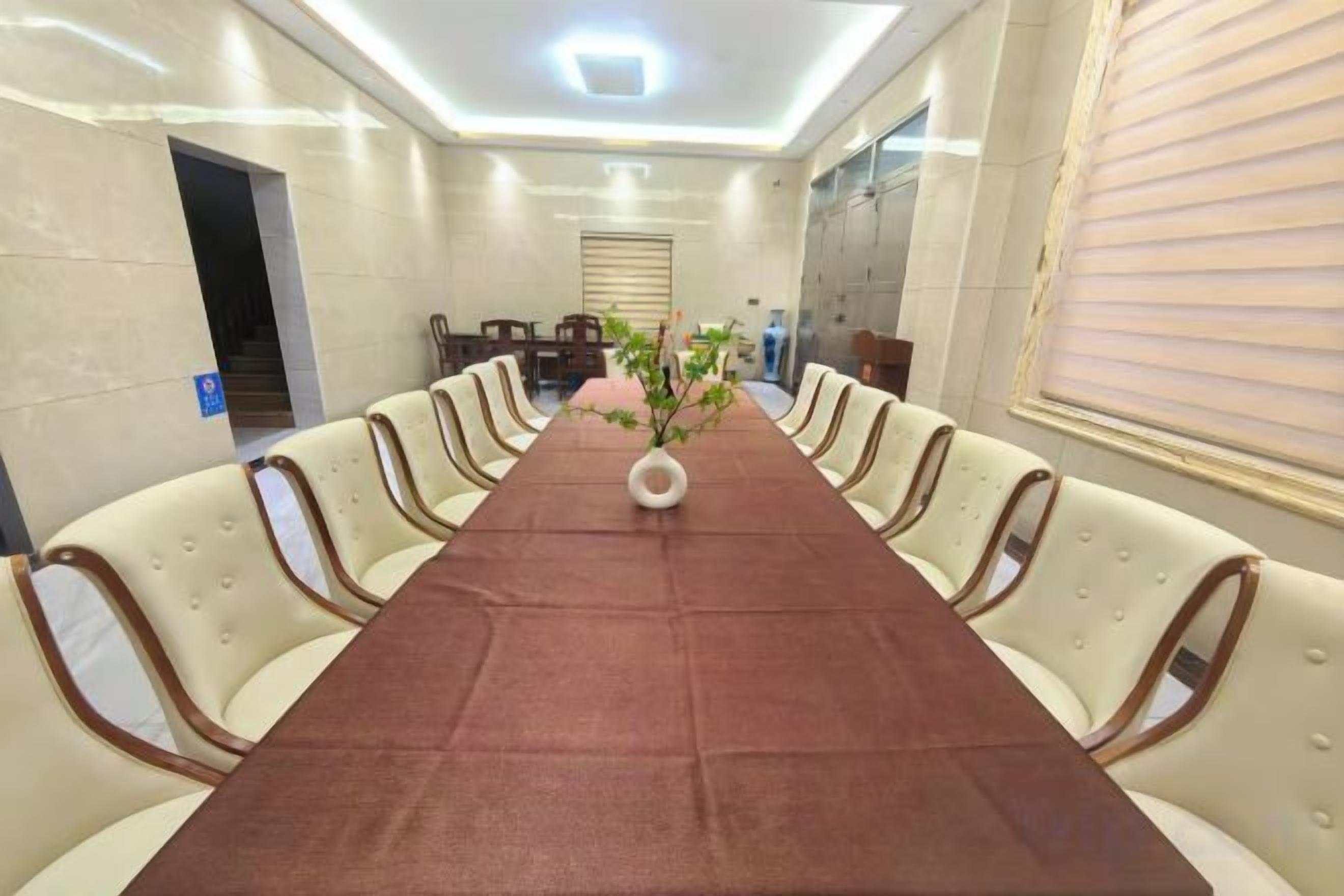 Un salón de conferencias con una larga mesa, sillas color beige y un jarrón con flores.