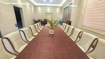 Un salón de conferencias con una larga mesa, sillas color beige y un jarrón con flores.