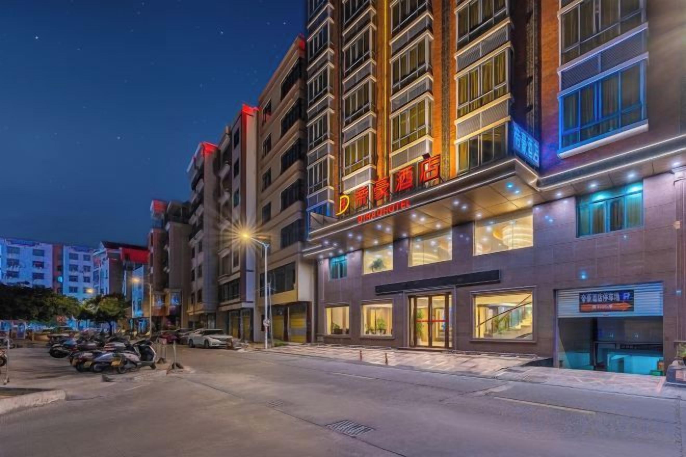 Un hotel de varios pisos con letreros iluminados, acceso a nivel de calle y un área de estacionamiento.