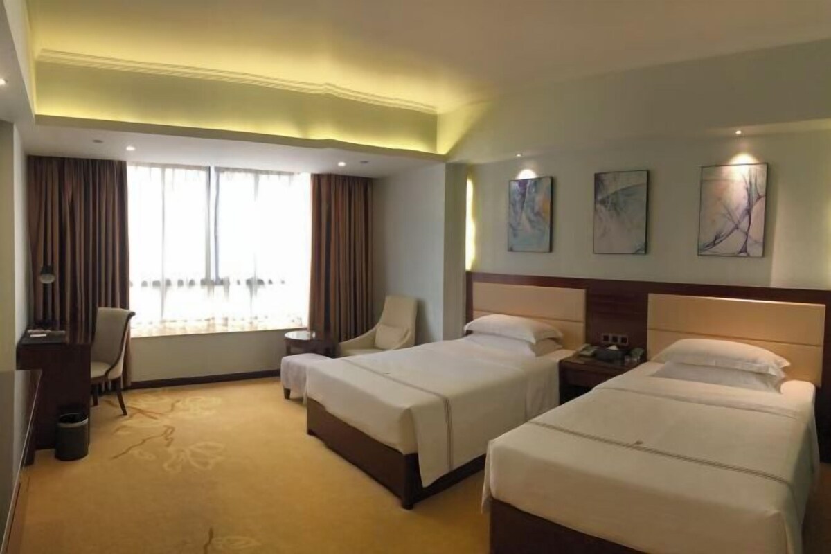 A hotel room with two beds, a desk, a chair, and a window with curtains.