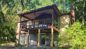 Une cabane à deux étages dotée d’un balcon, entourée d’arbres.