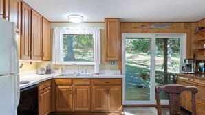 Une cuisine avec des meubles de rangement en bois, un réfrigérateur, un évier et une fenêtre donnant sur un jardin.