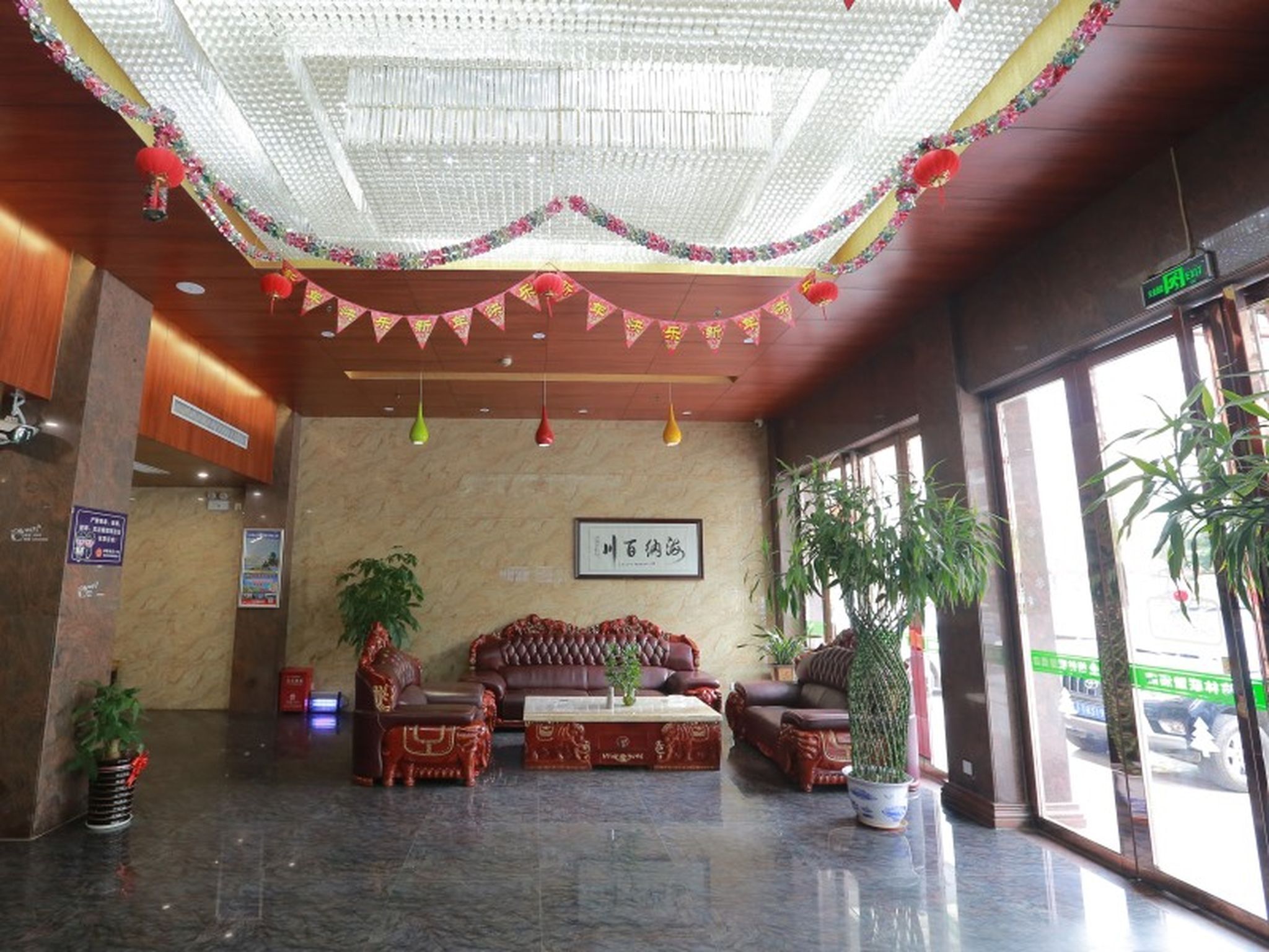 A lobby with a high ceiling, a sofa set, potted plants, and a sign on the wall.