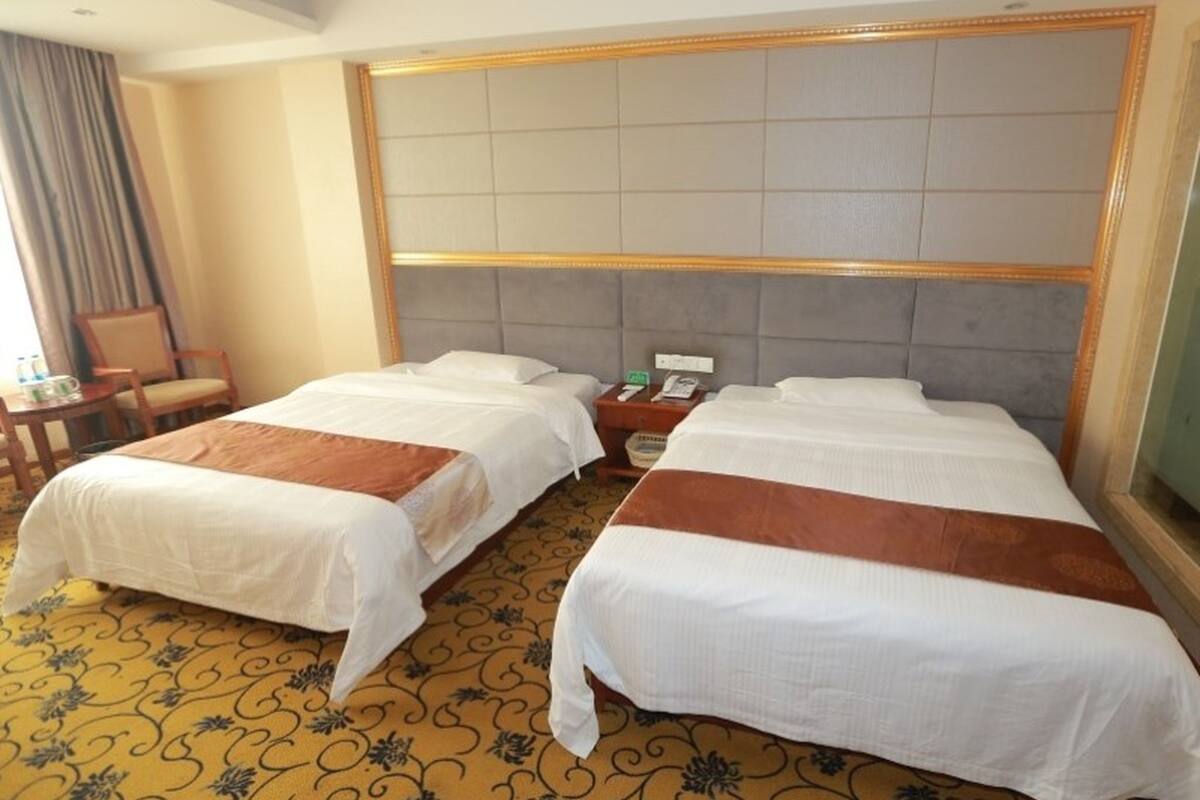 A hotel room with two beds, a headboard, a bedside table with a phone, and a chair.