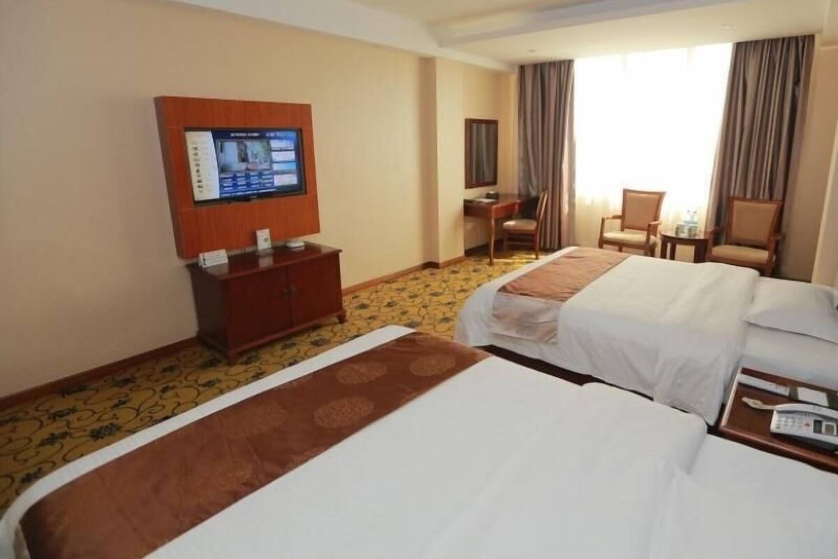 A hotel room with two beds, a desk, a chair, a TV, and a telephone.