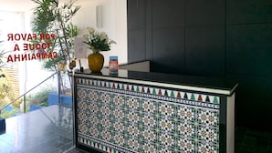 A reception area with a tiled wall, a potted plant, a sign, and a hanging light fixture. - Pousada Elxadai (Guarapari)