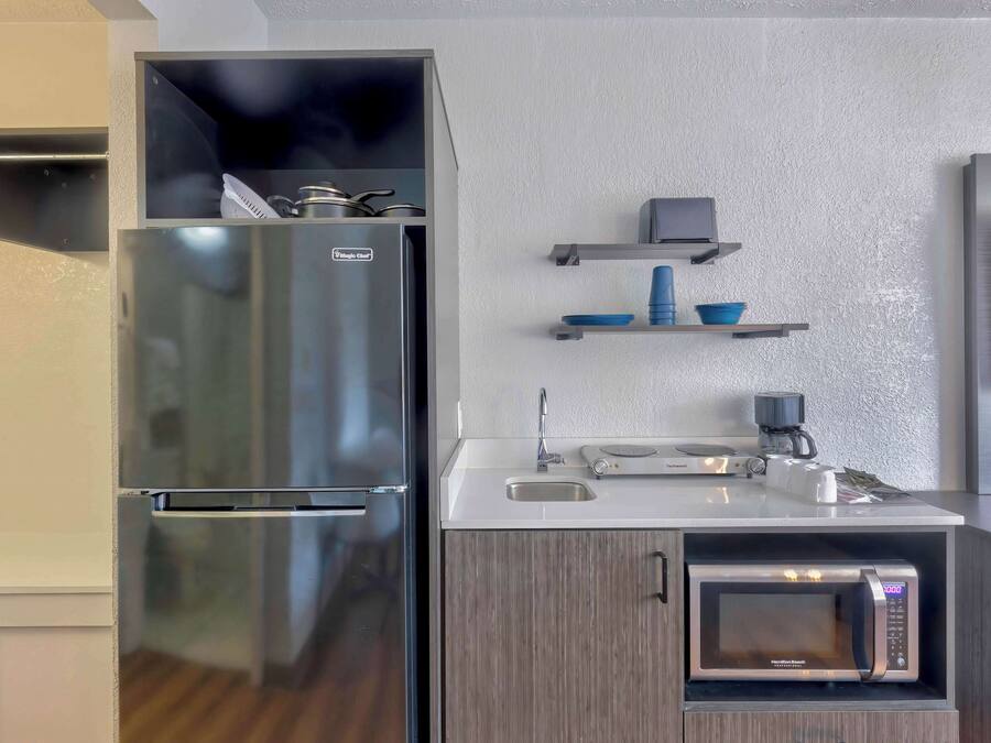 A compact kitchen with a stainless steel refrigerator, a microwave, and a coffee maker on the countertop.