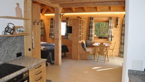 A wooden interior with a kitchen area, a dining table with chairs, and a bed with a window view. - Engadin Chalet Appartment- Val Bever St.Moritz ideal for 2 persons. New! (Bever)