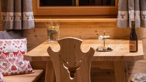 Een houten eettafel met een fles wijn, een glas water en een bord gebakjes. Er staat een stoel met een uitgesneden hert.