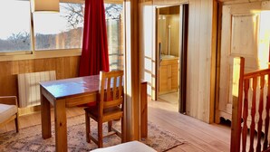 Un intérieur en bois avec une table à manger, des chaises, un rideau rouge et une vue sur l’extérieur.