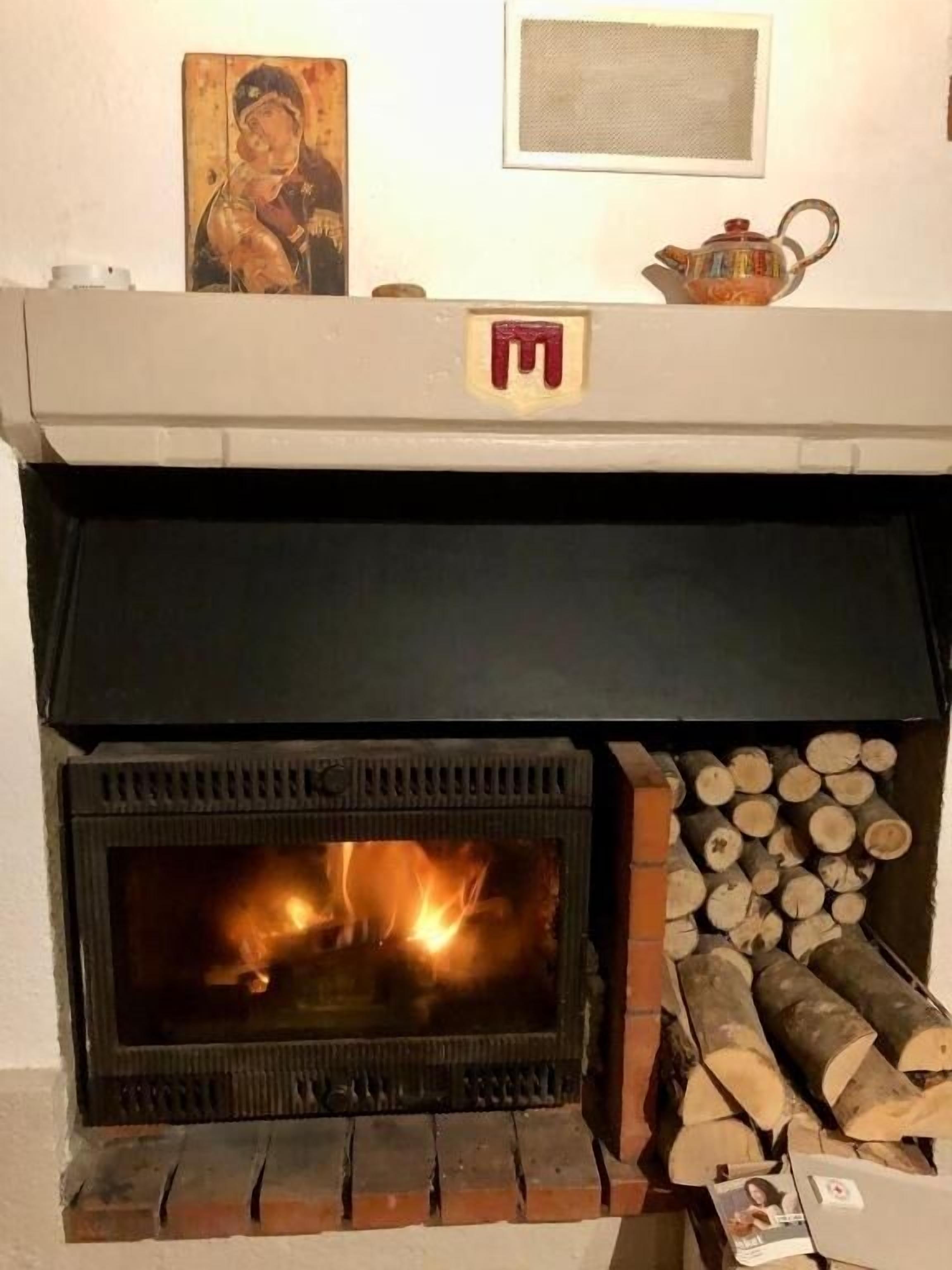 A fireplace with a fire burning, a stack of firewood, and a religious icon on the wall above the fireplace.