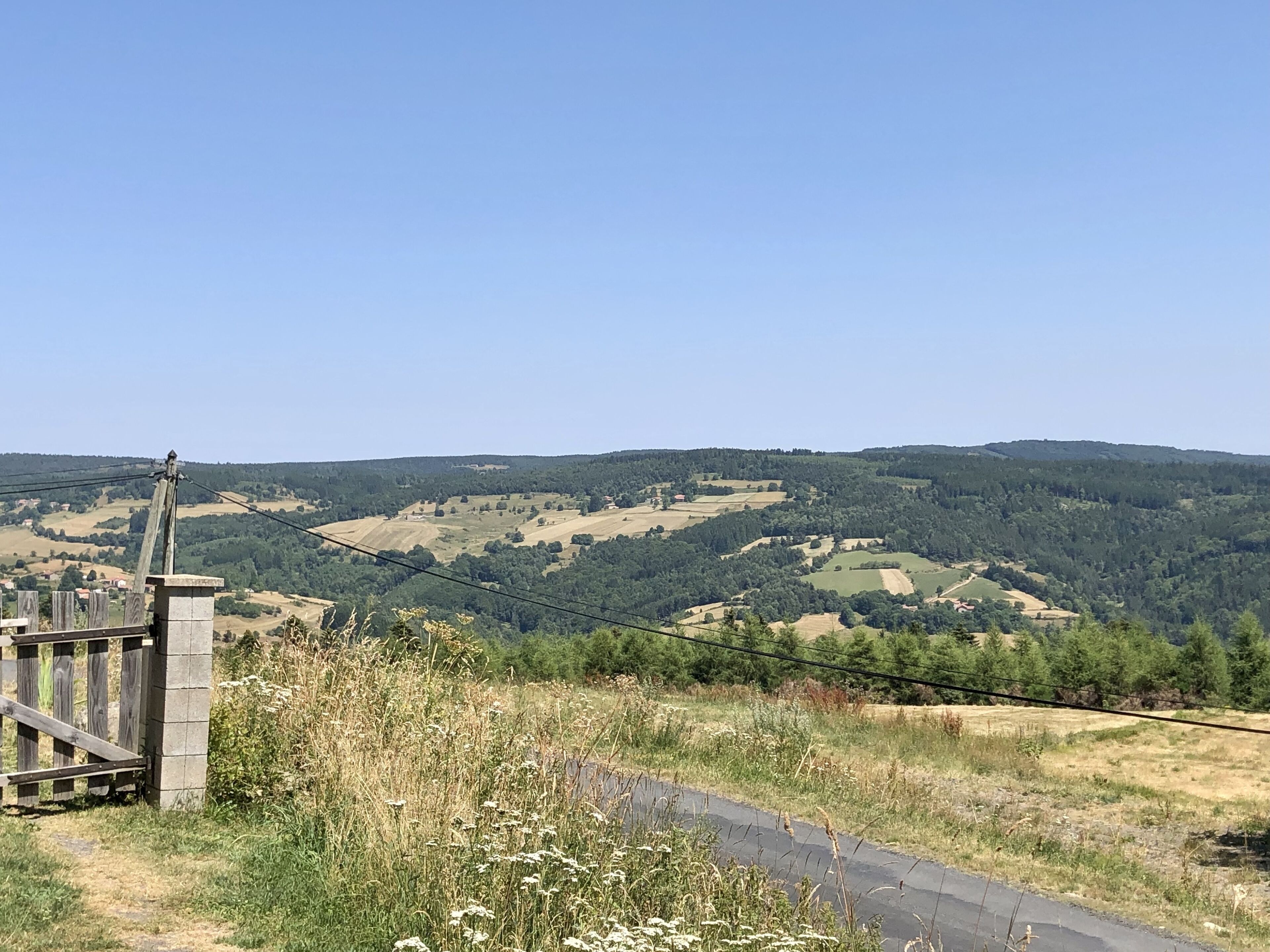 A rural landscape with a paved path, a wooden fence, and a stone structure.
