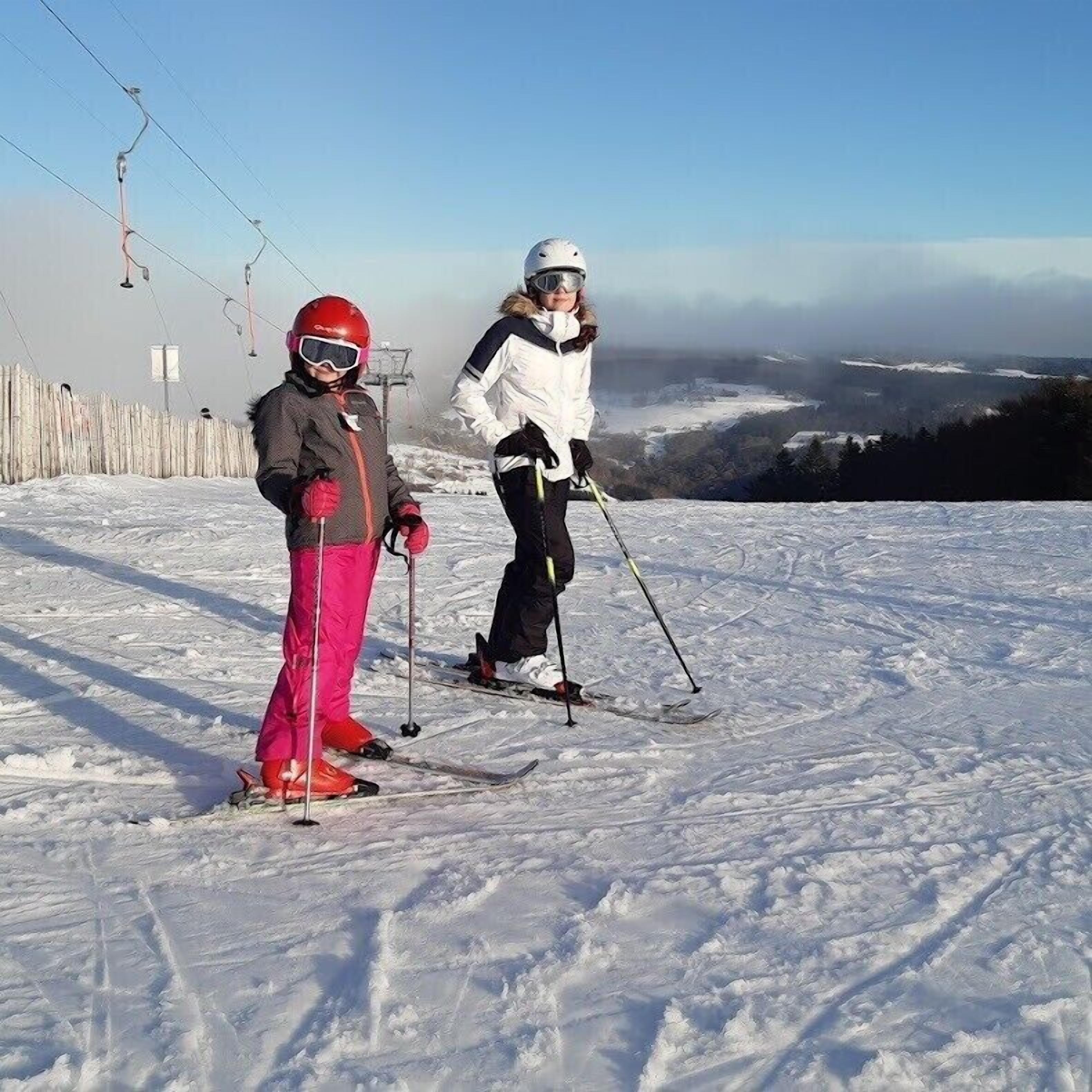 Two skiers on a snowy slope with a ski lift in the background.