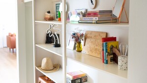 Una scaffalatura bianca con diversi oggetti, tra cui libri, un cappello, una valigia e soprammobili.